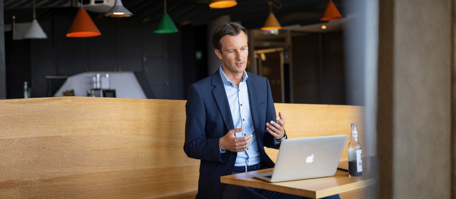 Carsten Tidow sits on a bench with his laptop open, gesturing as he explains.
