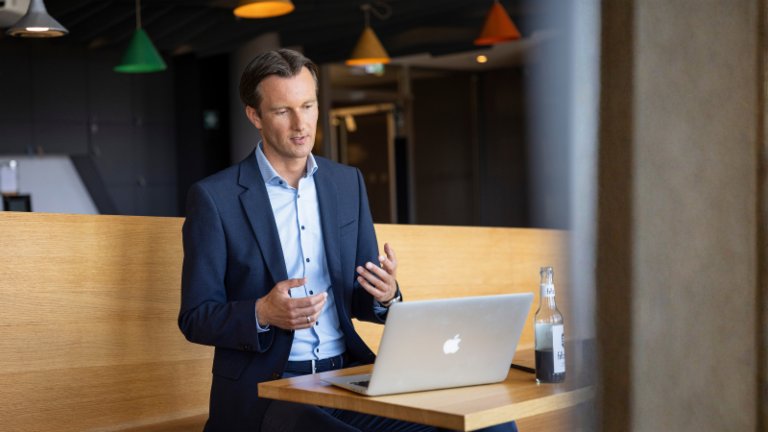 Carsten Tidow sits on a bench with his laptop open, gesturing as he explains.