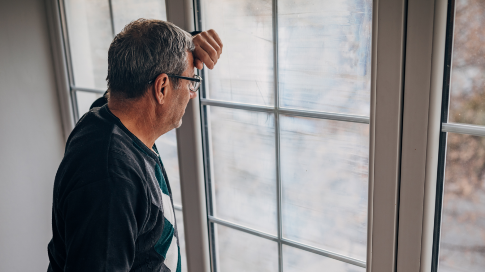 Fair debt collection: A middle-aged male debtor in an olive-colored jacket looks out the window with concern.