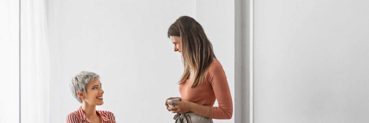 A younger woman talks to a sitting woman in front of a laptop 