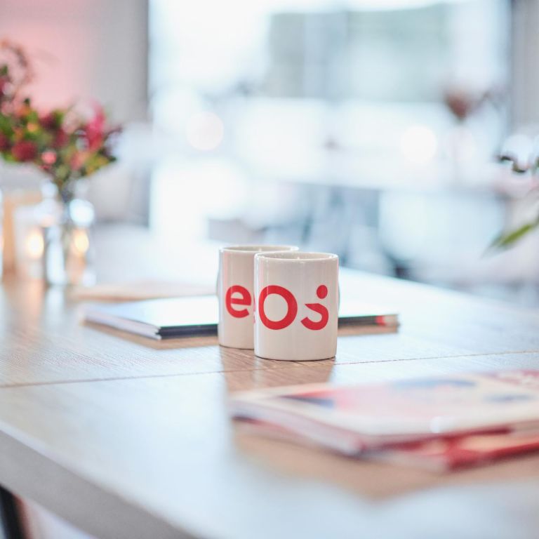 Two white cups with the new EOS logo are standing on a table