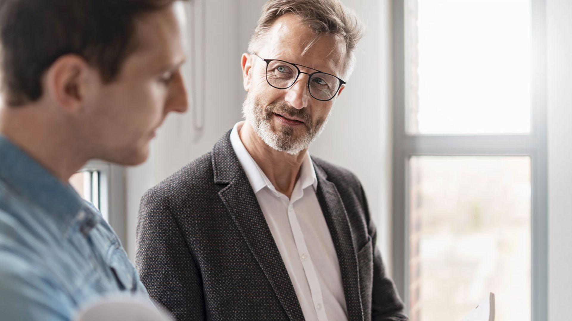 Two men in an office are discussing the results of the EOS Group's European Payment Practices 2025 study on digitization in receivables management.