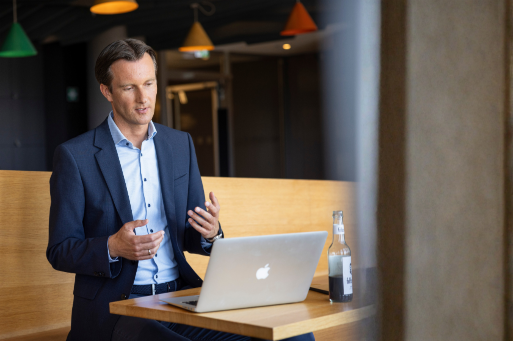 Carsten Tidow sits on a bench with his laptop open, gesturing as he explains.
